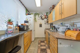 Útulná kuchyň s moderními prvky, dřevěnými skříňkami a dlažbou. Velká okna poskytují dostatek světla, zatímco vestavěné spotřebiče zajišťují pohodlí.