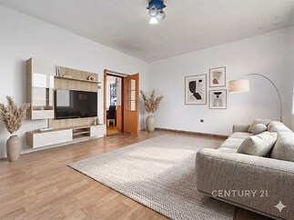 Světlý obývací pokoj s parketovou podlahou, moderní vestavěnou obývací stěnou a velkým šedým gaučem, který dodává místnosti elegantní vzhled.