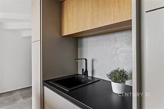Malá moderní kuchyň, matná skříňka, černé pracovní desky, dřevěné povrchy, minimalistický design.