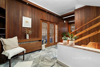 Vstupní hala s elegantní dlažbou a tmavými dřevěnými obklady, moderní styl, světlá výmalba a dřevěné schodiště vytvářejí útulný prostor.