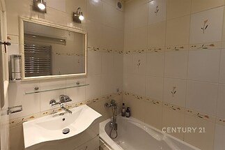 Koupelna s keramickými obklady, vanou a moderní sanitou, doplněná zrcadlem a osvětlením. Světlý a funkční prostor.
