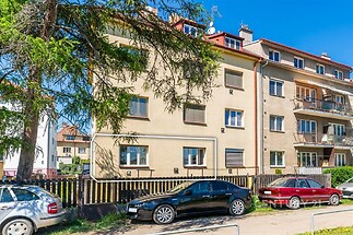 Bytový dům s rekonstruovanou fasádou, velkými okny a parkovacími místy před budovou, v klidné rezidenční čtvrti