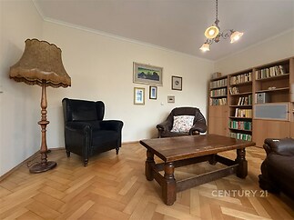 Obývací pokoj s parketovou podlahou, dřevěným nábytkem a vestavěnými knihovnami. Klasický styl a světlé stěny dodávají prostoru útulnost.