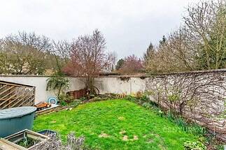 Zahrada s udržovaným trávníkem, obklopená vzrostlými stromy a keři, nabízí pohodlný prostor pro relaxaci.