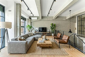 Světlý obývací pokoj s parketovou podlahou, moderní nábytkem a velkými okny. Industrální styl s betonovými stěnami a stropními nosníky.