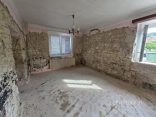 Prázdný pokoj s kamennými zdmi, velkým oknem a betonovou podlahou, vhodný k rekonstrukci, s výhledem do zahrady, dobrou vstupní investicí.