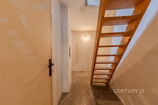 Úzké schodiště s dřevěnými schody vede do horního patra, cihlové stěny a dlažba na podlaze vytvářejí rustikální atmosféru v renovovaném prostoru.