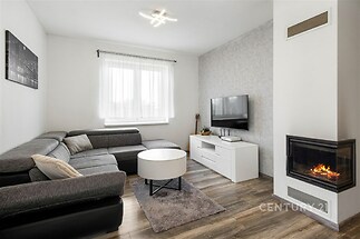 Moderní obývací pokoj s parketovou podlahou, krbovými kamny a světlým nábytkem, poskytující útulnou atmosféru a moderní styl bydlení.