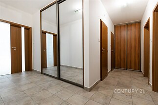 Chodba s dlažbou, vestavěnými skříněmi a dřevěnými dveřmi nabízí moderní design a dostatek úložného prostoru.