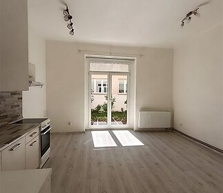 Prostorný obývací pokoj s moderní kuchyní, parketová podlaha, velká okna, světlý interiér, rekonstruovaný prostor.