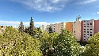 Pohled na sídliště s panelovými domy obklopené zelení, klidná lokalita, dostupné městské služby, vhodné pro rodinné bydlení.