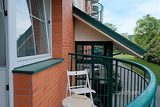 Moderní balkon s cihlovou stěnou, zeleným zábradlím a výhledem na svěží zahradu, ideální pro relaxaci v přírodě.