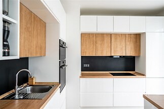 Moderní kuchyň s dřevěnými pracovními deskami, vestavěnými spotřebiči a světlými skříňkami, minimalistický design a funkční uspořádání.