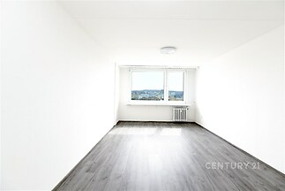 Světlý obývací pokoj s parketovou podlahou, velká okna s výhledem, moderní minimalistický design v nově rekonstruovaném bytě.