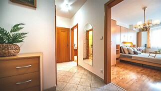 Vstupní chodba s dlažbou a zrcadlem, vedoucí do světlé ložnice s parketovou podlahou a vestavěnými skříněmi, v moderním stylu.