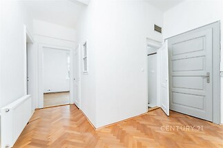 Prostorná chodba s parketovou podlahou a moderními dveřmi, vedoucí do světlých místností.