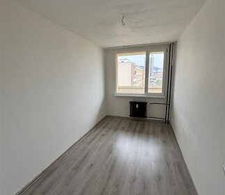 Úzká ložnice s parketovou podlahou a velkým oknem, které poskytuje výhled na město, vhodná pro moderní bydlení v rekonstruovaném bytě.