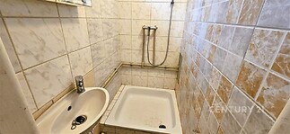 Kompaktní koupelna s dlažbou, sprchovým koutem a umyvadlem, ideální pro menší byt, vyžaduje modernizaci.