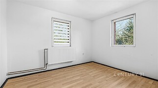 Světlý pokoj s laminátovou podlahou, dvě velká okna a radiátor, ideální pro moderní rekonstrukci nebo úpravy podle vlastních představ.