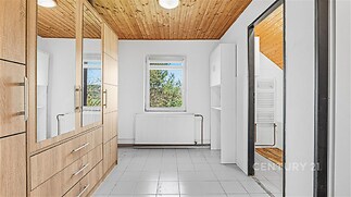 Předsíň s dlažbou, vestavěnými skříněmi a dřevěným obložením stropu poskytuje moderní úložné řešení a světlý prostor.