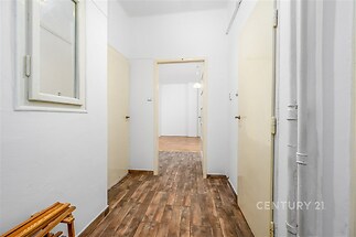 Úzká chodba s dlažbou imitující dřevo, světlé stěny a dveře vedoucí do obývacího pokoje, nabízí světlo a přístupnost v moderním stylu.