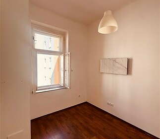Světlá ložnice s parketovou podlahou, velká okna zajišťující dostatek přirozeného světla, moderní minimalistický styl.