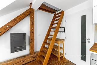 Podkrovní prostor s dřevěným schodištěm, parketová podlaha a bílá stěna s moderními prvky vytváří útulný a stylový interiér.