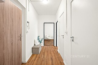 Chodba s moderními dřevěnými podlahami, světlými stěnami a elegantními dveřmi. Dekorativní prvky přidávají stylový nádech.