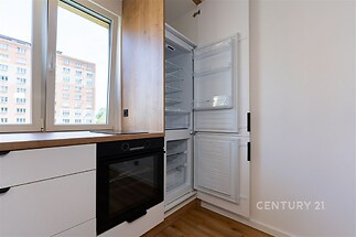 Moderní kuchyň s dřevěnou podlahou, vestavěnou troubou a lednicí. Světlý interiér s velkými okny přináší přirozené světlo.