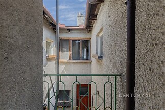 Úzký venkovní prostor s betonovými stěnami, dřevěnými prvky a modrou oblohou. Styl historický, vhodný pro rekonstrukci nebo přestavbu.