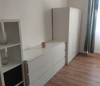 Světlá ložnice s dřevěnou podlahou, moderním nábytkem a vestavěnými skříněmi, vybavená velkými okny pro dostatek přirozeného světla.