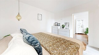 Světlá ložnice s parketovou podlahou, moderním nábytkem a dekorativními prvky, prostorná a útulná atmosféra.