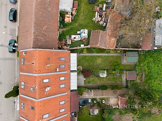 Pohled na prostornou zahradu se zeleným trávníkem a dřevěnými přístřešky, obklopenou domy s červenou taškovou střechou, ideální pro rekreační využití