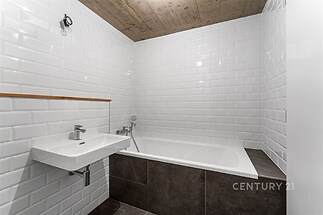 Koupelna s moderní dlažbou, bílými obklady a dřevěným stropem, vybavená vanou a umyvadlem.
