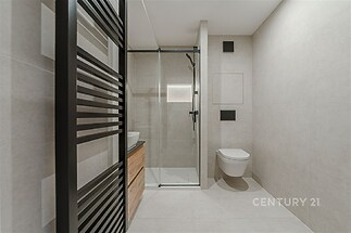 Moderní koupelna s dlažbou, sprchovým koutem a závěsnou toaletou. Minimalistický design s čistými liniemi a světlou povrchovou úpravou.