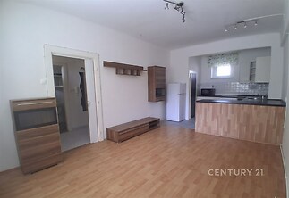 Obývací pokoj s parketovou podlahou a moderním kuchyňským koutem. Světlé stěny a dřevěný nábytek vytvářejí příjemnou atmosféru.