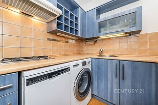 Malá kuchyň s modrými skříňkami, dlažbou a vestavěnými spotřebiči. Pracovní deska z dřeva opticky zvětšuje prostor.