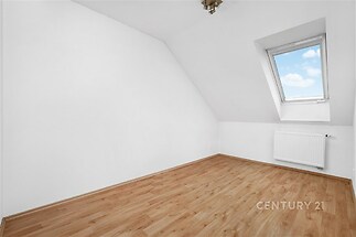 Podkrovní pokoj s laminátovou podlahou, střešním oknem a bílými stěnami, světlý prostor vhodný pro moderní bydlení