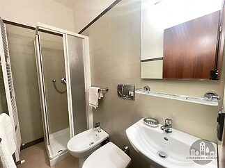 Koupelna s dlažbou, sprchovým koutem a moderními sanitárními prvky, vybavená bílým umyvadlem a bidetem, sofistikovaný design a praktické úložné prostory.