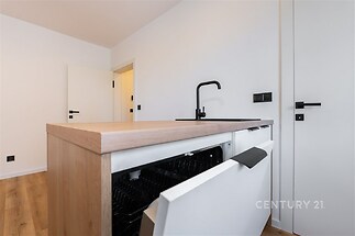 Moderní kuchyň s dřevěnou pracovní deskou, parketovou podlahou a vestavěnou myčkou; minimalistický design a čisté linie.