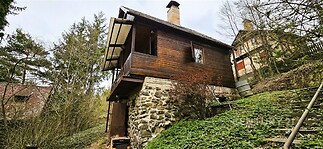 Horská chata s dřevěnou fasádou a kamenným základem, obklopená přírodou. Rustikální styl, útulné útočiště v přírodě.