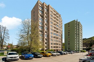Výšková obytná budova s panelovou strukturou, modernizovaná, s výbornou dostupností a blízkostí zeleně, parkující automobily před domem.