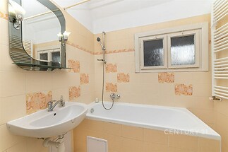 Koupelna s dlažbou a vanou, vybavená umyvadlem se zrcadlem a topným žebříkem, nabízí světlý a udržovaný prostor vhodný k renovaci.