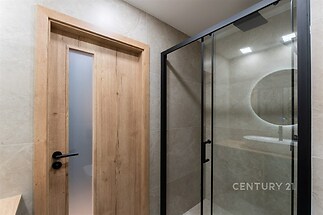 Moderní koupelna s elegantní dlažbou, sprchovým koutem s prosklenými dveřmi a dřevěným obkladem, vytvářející minimalistický vzhled.