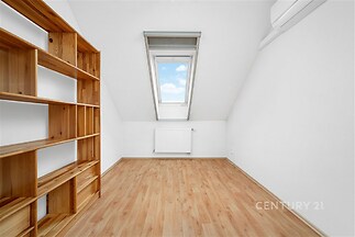 Podkrovní pokoj s laminátovou podlahou, velkým střešním oknem a vestavěnou dřevěnou knihovnou, světlý a prostorný interiér vhodný pro moderní bydlení.