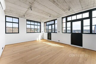 Světlý obývací pokoj s parketovou podlahou a velkými okny, moderní průmyslový styl s betonovým stropem a výhledem na město.