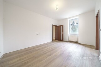 Prázdný pokoj s parketovou podlahou a velkým oknem, moderní styl a bílá výmalba, ideální pro kreativní využití prostoru.