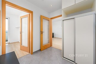 Světlá vstupní chodba s dlažbou, moderní vestavěné skříně a dřevěné dveře, propojená s obývacím pokojem a ložnicí, ideální pro rodinné bydlení.