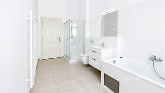 Světlá koupelna s moderními prvky, jako je sprchový kout, vana a dlažba. Prostorná dispozice a elegantní bílý nábytek zajišťují komfort.