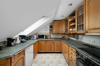 Podkrovní kuchyň s dřevěnými skříňkami, dlažbou a velkým střešním oknem, které zajišťuje dostatek světla, působí útulně a moderně.